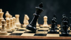 一個倒下的黑色國王棋子在木板上，附近有白色棋子。