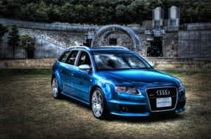 閃亮的藍色 Audi RS4 Avant 停在石頭圓形劇場附近的草地上（日落時分）。 — Surface Pro 壁紙