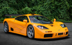 橙色McLaren F1 GTR跑車停在瀝青路上，後面有綠樹。 — Steam Deck 壁紙