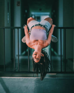一位女子倒掛在城市走廊的欄杆上微笑。