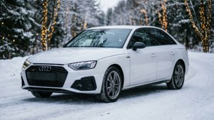白色奧迪轎車停在雪路上，冬季森林中樹木亮起燈光