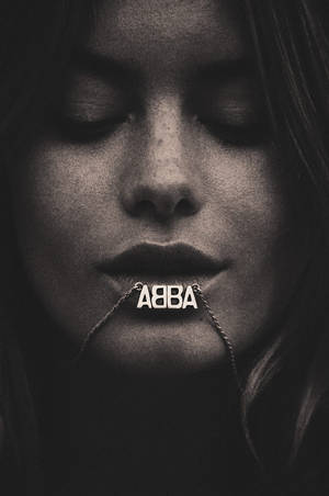 閉上眼睛的女性特寫肖像，戴著帶有 ABBA 文字的鏈條。