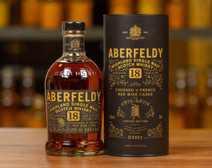 Aberfeldy 18年威士忌酒瓶和盒子放在木桌上，後面有模糊的琥珀色瓶子。