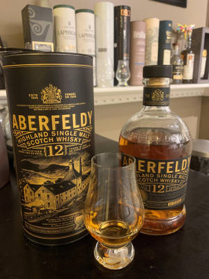Aberfeldy 12年威士忌酒瓶和品酒杯在深色桌子上，帶有品牌包裝。