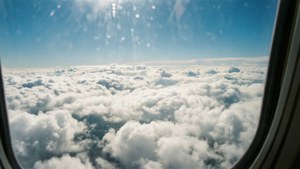 從飛機窗戶俯瞰蓬鬆白雲的空中景色，明亮的藍天和太陽耀斑