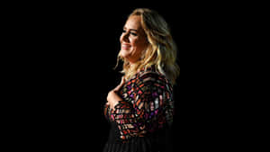 Adele 著住閃爍上衣，喺黑色背景前微笑。