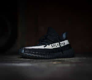 昏暗光線下，混凝土地板上的黑色Yeezy Boost 350運動鞋，帶有白色條紋。