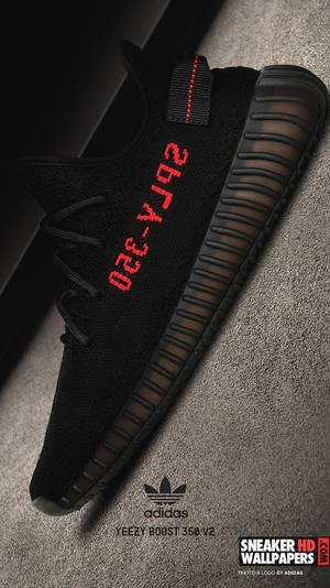 灰色地毯上的黑色Yeezy Boost 350 V2運動鞋，帶有紅色文字。