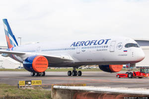 俄羅斯航空飛機在機場停機坪上，帶有橙色引擎罩，附近有地勤車輛。