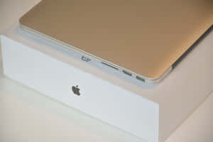 金色 MacBook 放在白色 Apple 盒上，顯示連接埠和標誌