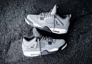 灰色Jordan 4運動鞋搭配白色鞋底，位於深色瀝青表面。