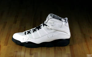 白色 Air Jordan 12 運動鞋，帶有黑色細節，置於木地板上。