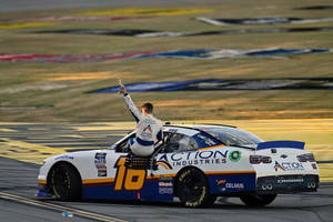 NASCAR車手在日落時分在賽車上舉起獎盃慶祝勝利。