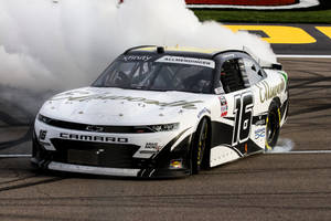 白色和黑色的 NASCAR 賽車在賽道上冒煙漂移。