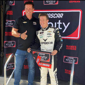 兩位男士喺NASCAR Xfinity Series頒獎台上，一位著住賽車服拎住獎項，另一位豎起拇指。