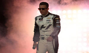 NASCAR車手身穿賽車服在夜間明亮的燈光下穿過煙霧。