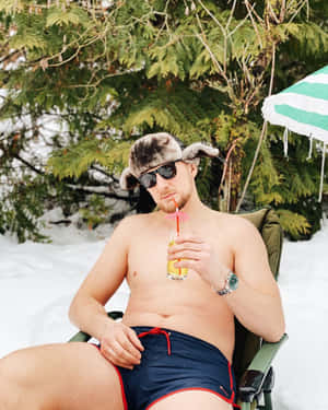 穿著泳褲和毛帽的男人在雪地森林中撐傘喝飲料。
