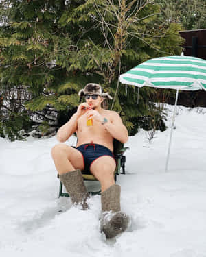 穿泳褲和帽子的男人在雪地後院用傘喝飲料。
