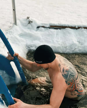 有紋身的男子在白雪皚皚的冬日景色中用藍色梯子從冰水中爬出。