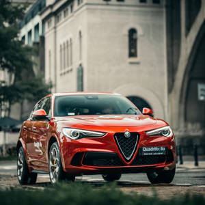 紅色愛快羅密歐 Quadrifoglio 賽車停泊在歷史建築附近的鵝卵石街道上。