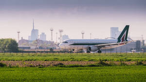 意大利航空飛機在跑道上，背景有綠色田野和城市天際線