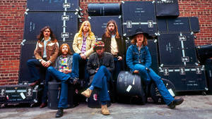 Allman Brothers Band 的六位音樂家坐在設備箱上，背靠磚牆。 — 音樂 GIF 壁紙