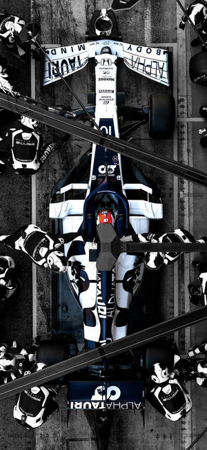 Formula 1 race car with pit crew surrounding it on track.