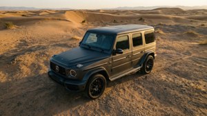 啞光黑色Mercedes G-Class SUV在日落時停放在沙漠沙丘上。