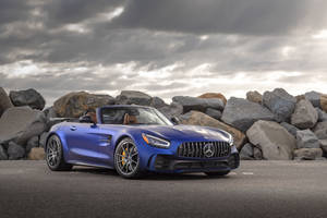 藍色 Mercedes-AMG GT R 開篷車停泊在岩石附近，天空多雲。