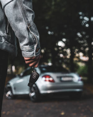 黃昏時分，人物手持平治車匙，背景有銀色汽車。