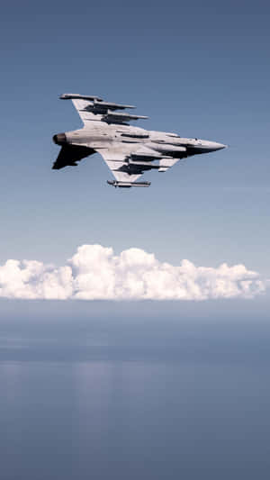 一架軍用噴射機在海洋上空的雲層上方飛行。 — 9:16 壁紙