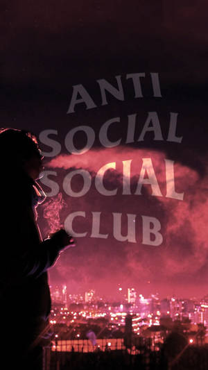 一個人在吸煙，'ANTI SOCIAL SOCIAL CLUB' 文字在夜晚的城市上空發出粉紅光芒。