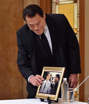 身穿黑色西裝的男子觸摸紀念桌上帶有水樽的裱框照片。 — 日本武士 壁紙