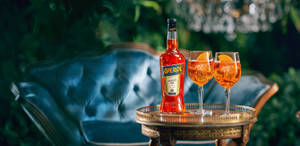 花園中藍色沙發旁的托盤上放著Aperol瓶和兩杯雞尾酒。 — Jugo GIF 壁紙
