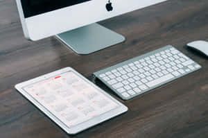 銀色 Apple iMac 鍵盤和 iPad 放在深色木桌上，日曆打開。