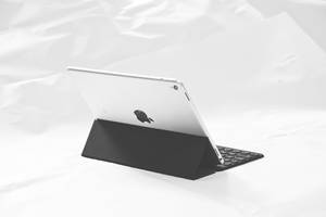 銀色 iPad 配鍵盤保護殼，背景為白色皺褶布料。