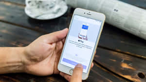 手在木桌上用iPhone使用Apple Pay，旁邊有咖啡和報紙。