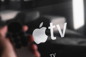 手持遙控器指向Apple TV屏幕，標誌對焦清晰。