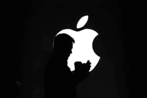 夜晚在發光Apple標誌前手持電話的人。