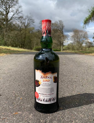 Ardbeg Scorch威士忌酒瓶置於道路上，有樹木和多雲天空。