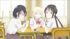 三個穿著校服的動漫女孩在教室桌上玩卡牌遊戲。