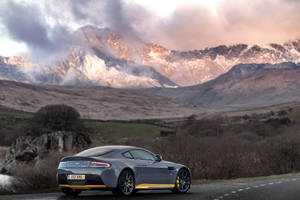 灰色 Aston Martin 跑車，帶有黃色飾邊，停泊在日落時分的山路上。