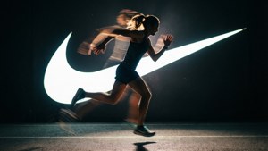 一名女性在夜間帶著動態模糊跑過一個明亮的Nike標誌。