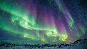 在星空下，綠色和紫色極光在雪覆蓋的山脈上閃爍