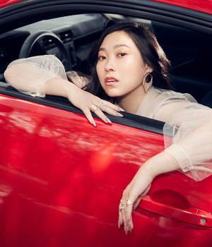 身穿透視襯衫的女性從紅色車窗探出身子，戴著金色耳環和戒指。 — 紅色美學 壁紙