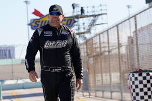 NASCAR車手BJ McLeod身穿黑色賽車服和太陽眼鏡在賽道上行走。 — 黑色動態圖 壁紙