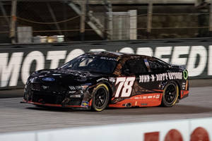 黑色和橙色的NASCAR賽車在夜間賽道上疾馳。