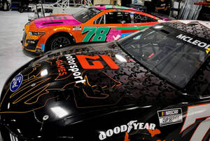 兩輛帶有鮮豔貼花的NASCAR賽車停放在車庫中。 — 黑色動態圖 壁紙