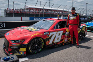 NASCAR車手身穿紅色賽車服在賽道上與賽車合影。