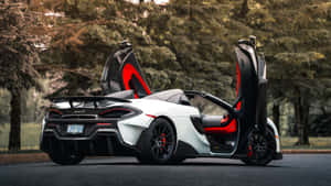 白色McLaren跑車，紅色內飾，打開車門，停泊在樹木環繞的瀝青路上。 — 5120x2880 壁紙